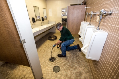 Plumber using a drain snake to clear a clog in a public bathroom